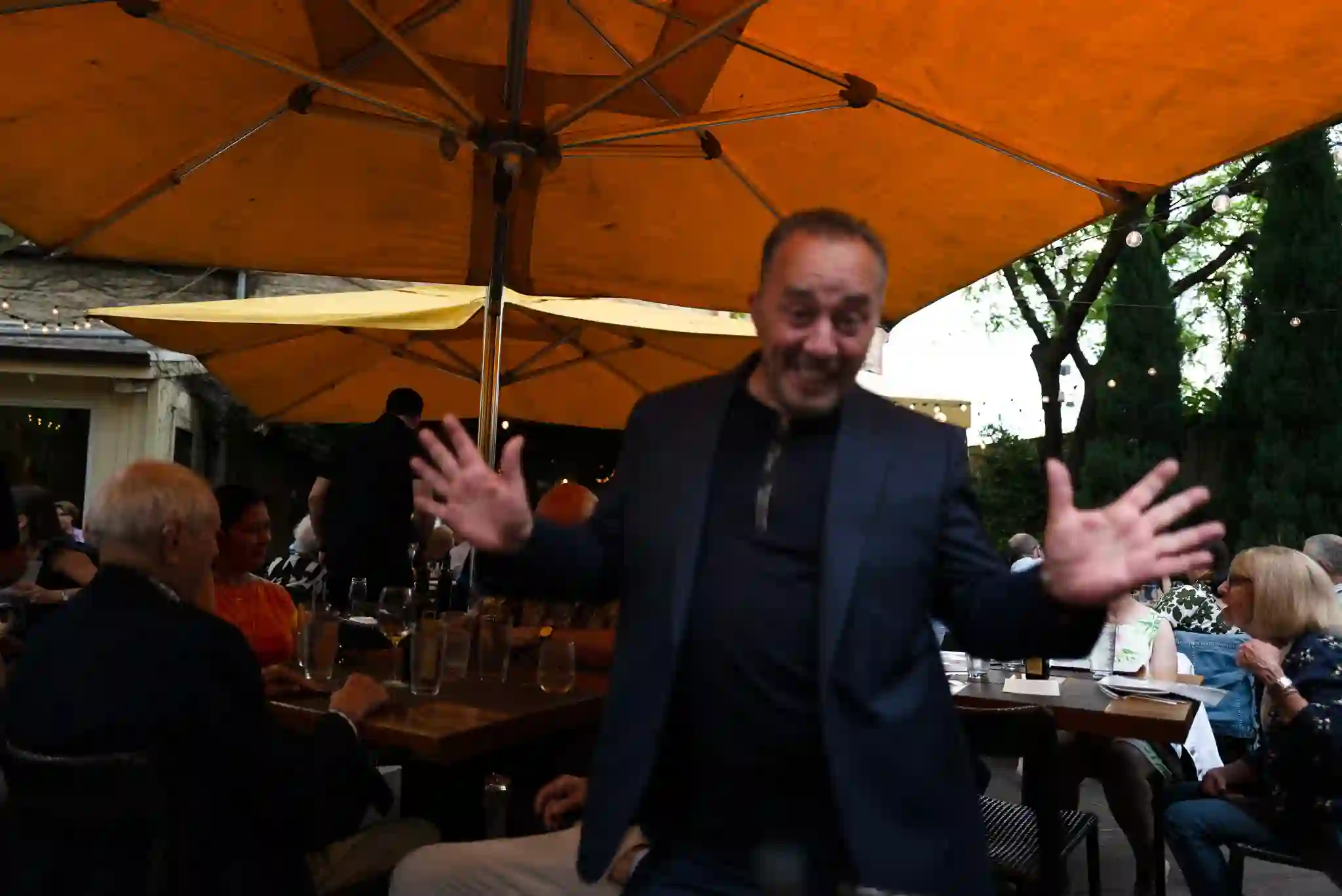 Host mid-story on the patio under the orange umbrellas